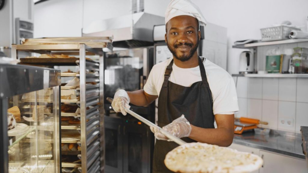 A Person Placing a Pizza Into the Oven Using a Pizza Peel