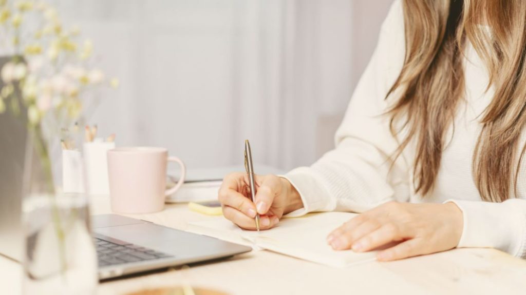 Hands of a woman writing while working on a laptop