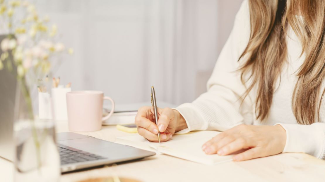 Hands of a woman writing while working on a laptop